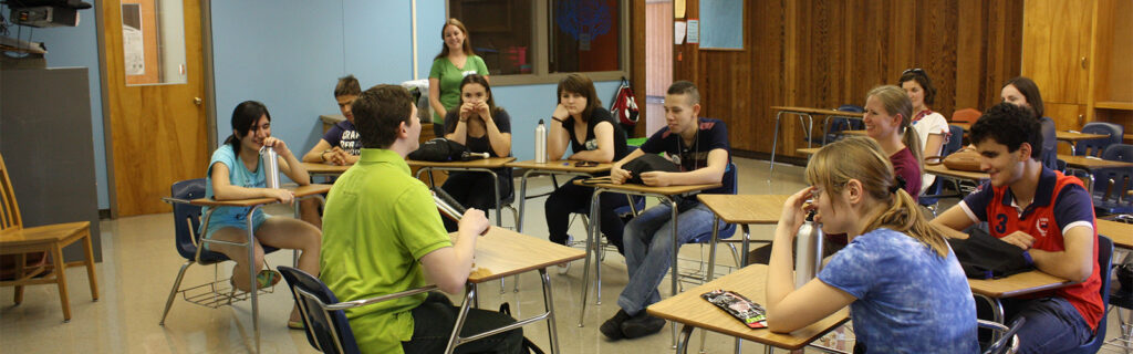 High school students sit in a semi-circle in a classroom.