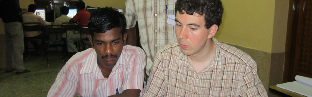 Robert Thompson and two Indian men look at a video on a laptop