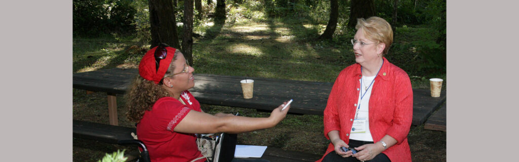 A woman in a red suitcoat listens intently to another woman talking