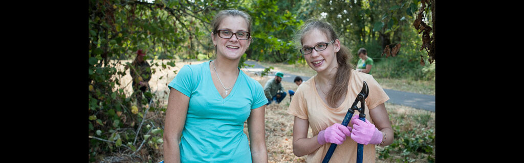 Two female exchange students smile at the camera in an outdoor setting.