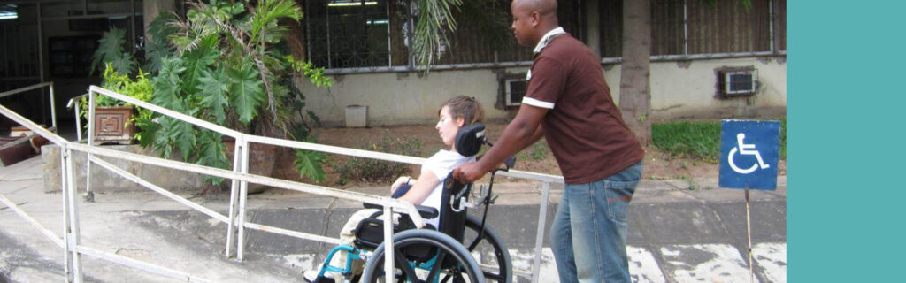 Pushing woman in wheelchair up a ramp.