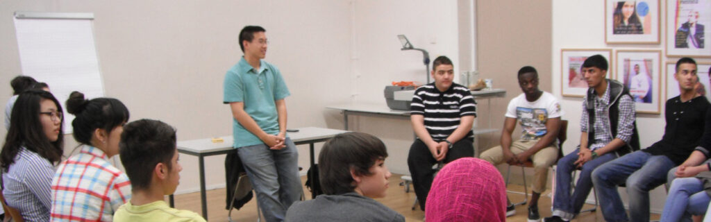 A group of students is seated in a circle around Samson as he teaches a class.