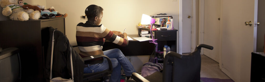 Young girl transfered from wheelchair to bedroom desk to study