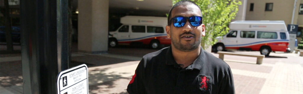 A young man wearing sunglasses outdoors next to a crosswalk button.