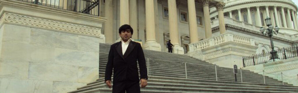 A young Pakistani man in a suit stands in front of the Capitol building in Washington, D.C.