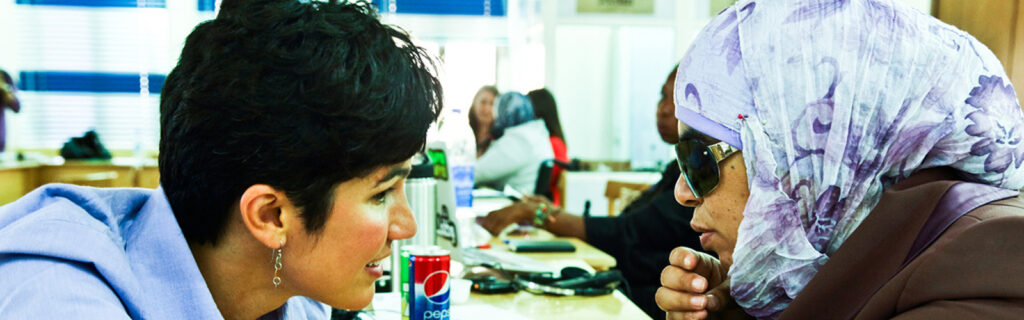 Two women, one with a head scarf, lean in to talk confidentially