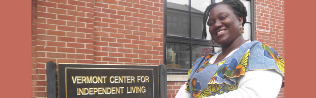 A smiling Ghanaian woman is near a building and sign that reads "Vermont Center for Independent Living."