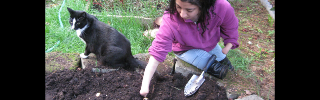 A young Pakistani girl with no legs or hands digs in a garden alongside a pet cat.