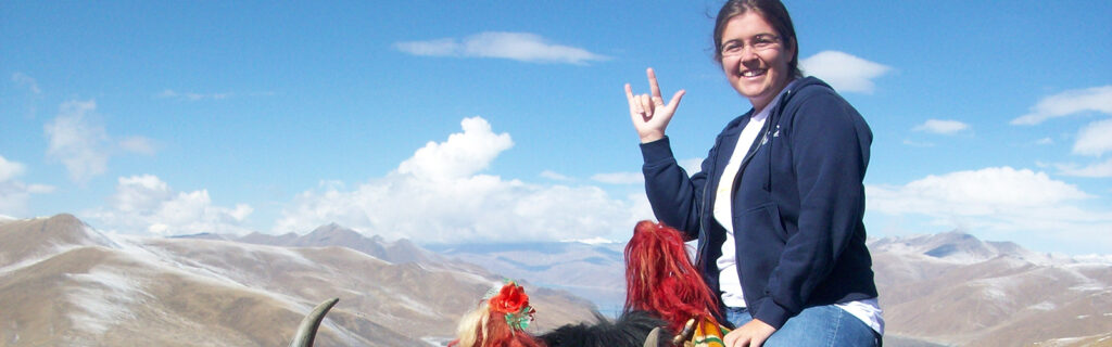 A young American woman seated on a yak signs "I love you" in sign language.