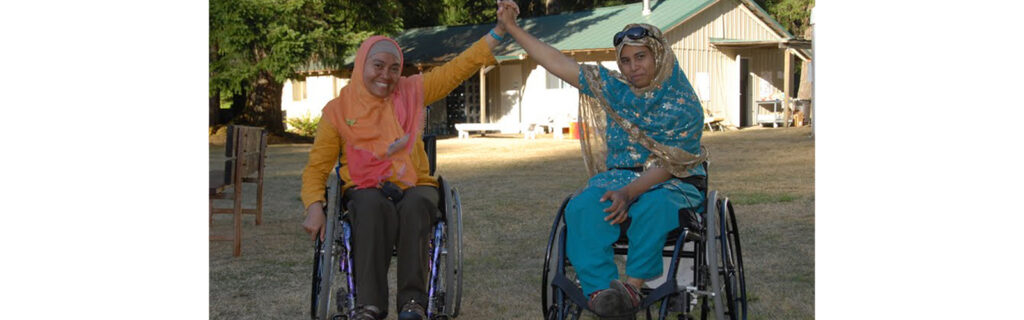 Two women in manual wheelchairs holding hands up in the air, one from Indonesia, the other from Bangladesh