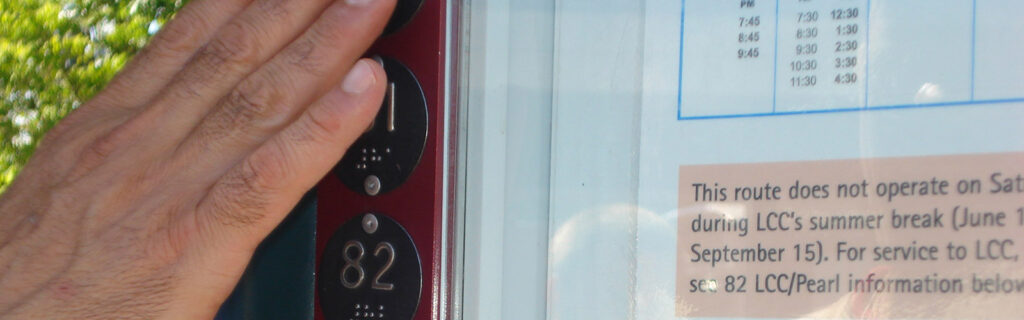 Hand of someone reading braille on the edge of a public bus posted schedule