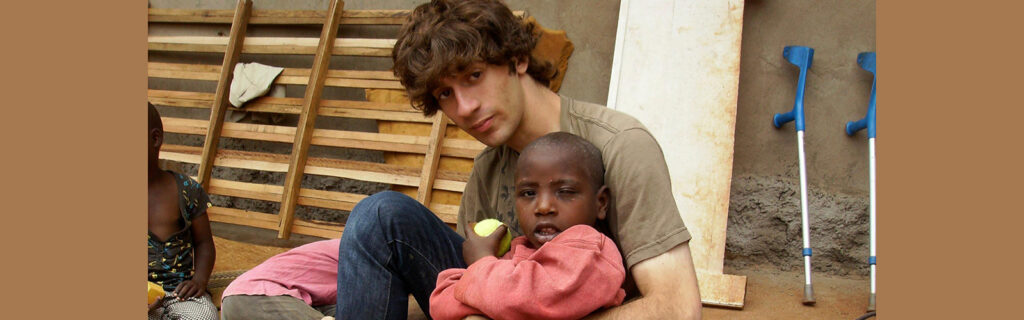 Zach sits on the ground with Ugandan child with a disability