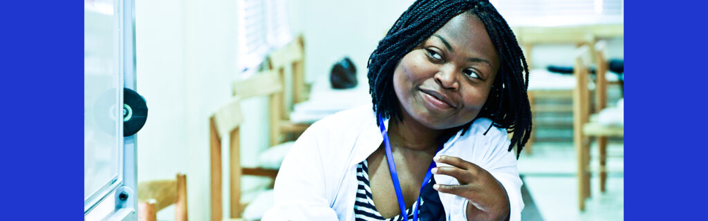 In a classroom, a black woman with physical disability smiles and listens to what you have to say