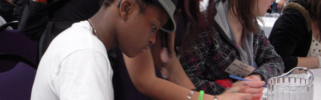 Student wearing a hearing aid writing in a classroom with other students.