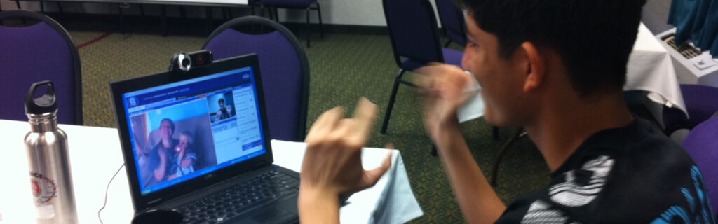 A teenage boy uses sign language with a person on a computer screen.