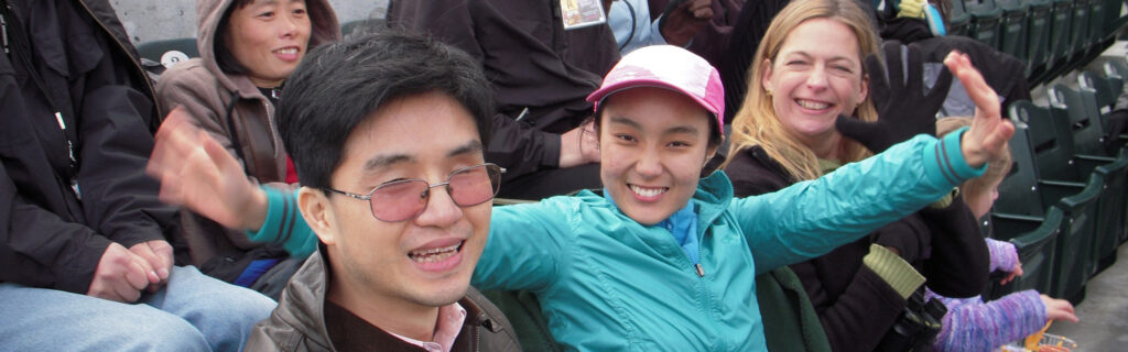 International students sitting and smiling on bleachers at sports game.