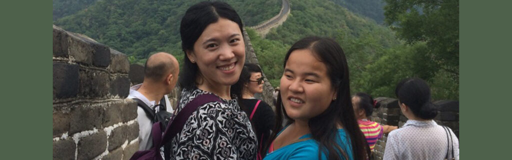 Two women (one is Hannah) look over their shoulders smiling. Great Wall of China is visible behind them.