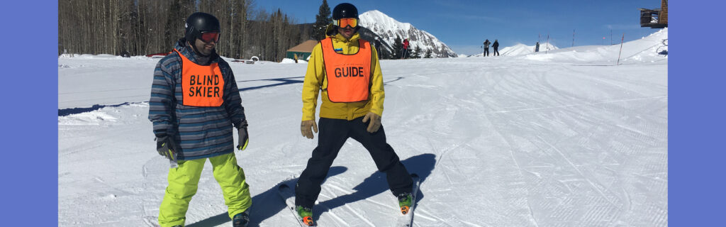 Noah wearing skis standing next to ski instructor in front of mountains.