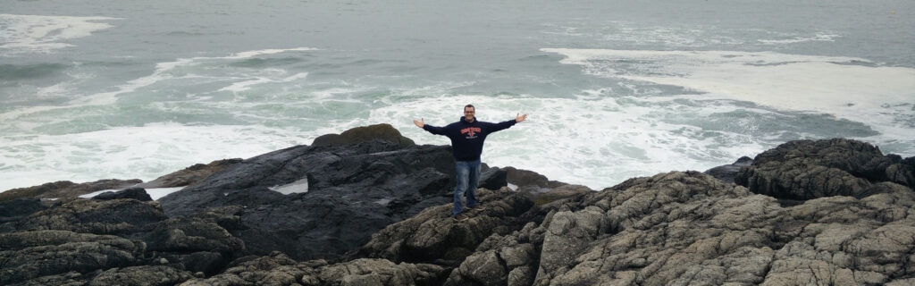 Distant view of a man standing on oceanside boulders with arms outstretched