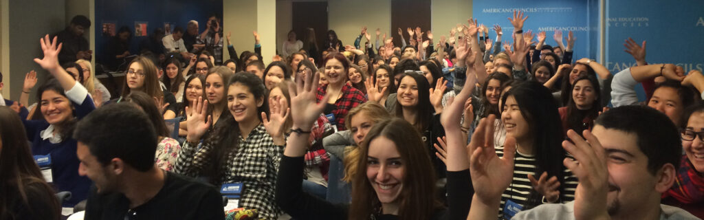 Group of students cheering with their hands raised in a conference room