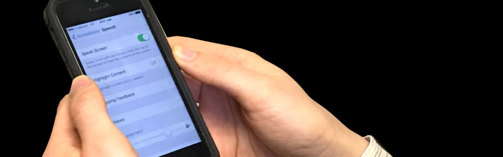 Hands holding an iphone with speech accessibility options on screen.