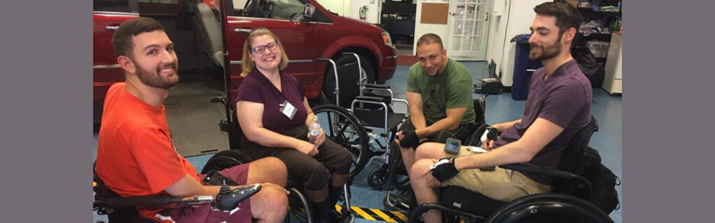 Stacy smiling in circle with group of 3 men, who are wheelchair riders, in front of an accessible van.