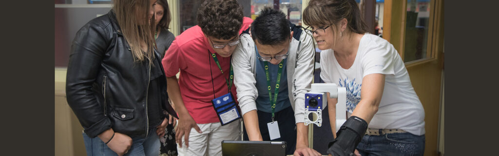 A teacher showing 3 international students a magnifier and iPad.