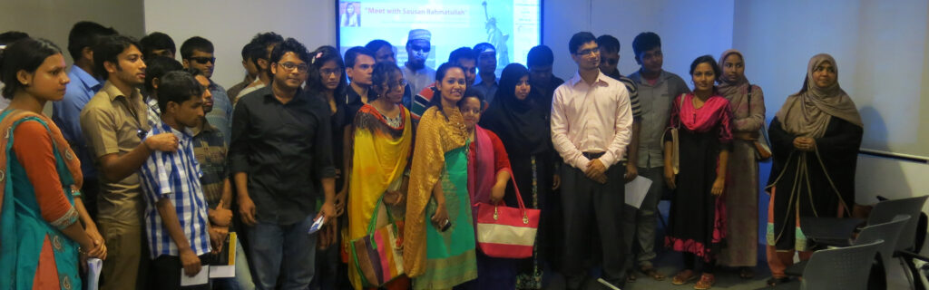 About two dozen Bangladeshi men and women stand in a room before a projector screen