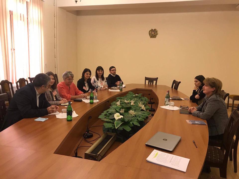 Six men and women sit at a boardroom table across from two women during a meeting