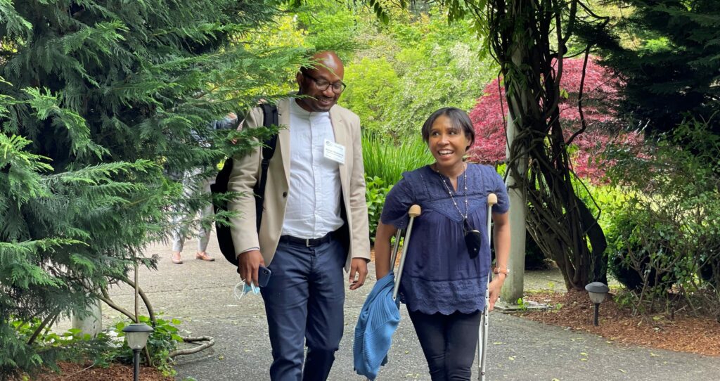 Cropped photo of two adults - a man and a woman - walking together through garden in conversation, one who uses crutches for mobility