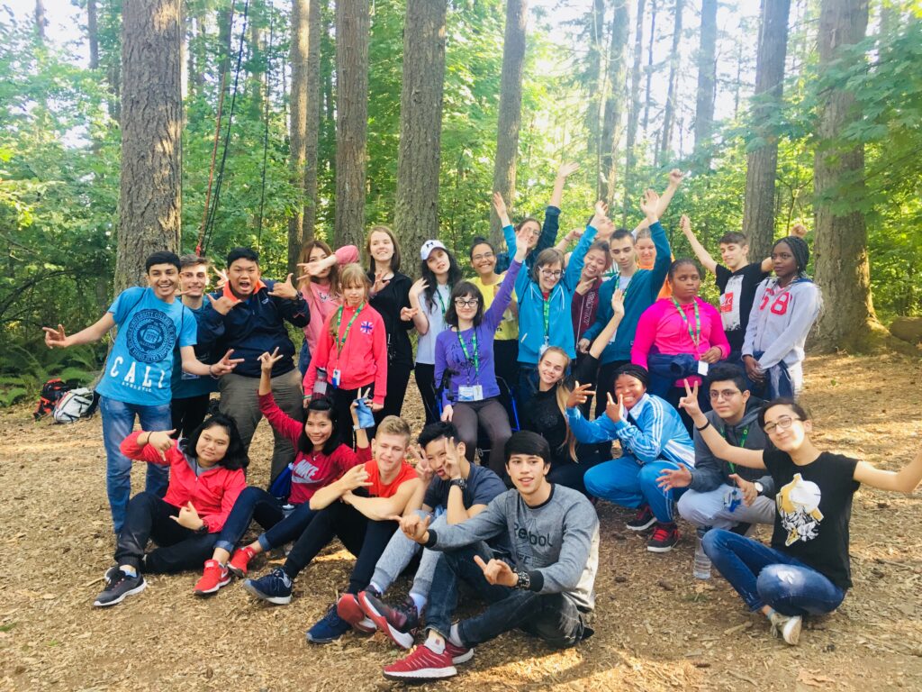 A large group of students pose, smiling, in a forest