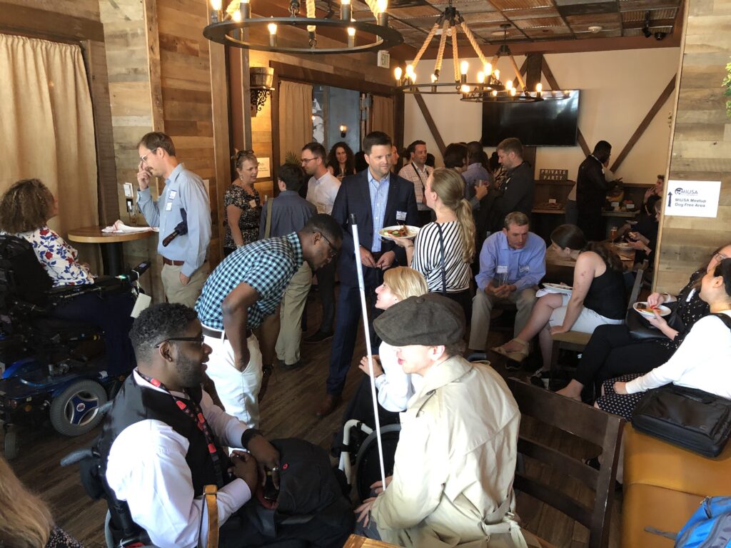 Large room with many people having engaging discussions, including many people with disabilities.