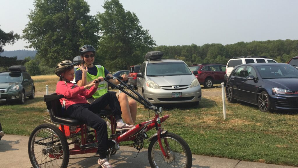 Two people ride on tandem bicycle on a paved path.