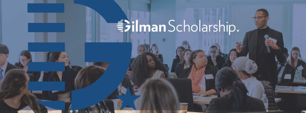 Man standing and speaking to a classroom; text "Gilman Scholarship" written over image.