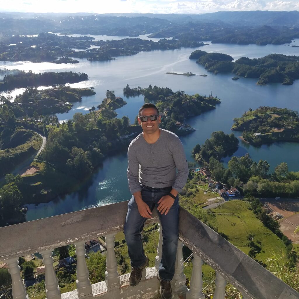 Anthony sits on a ledge, wearing sunglasses, overlooking green islands over water.