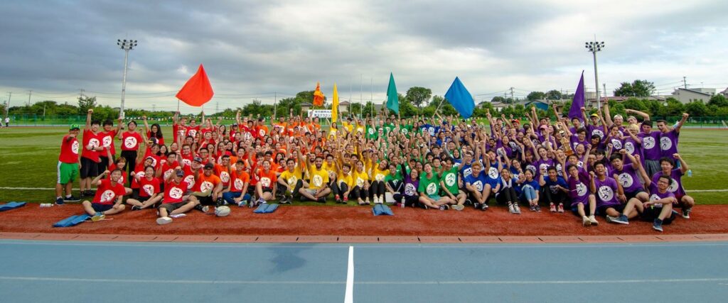 Panoramic photo of large group of students sitting on track.