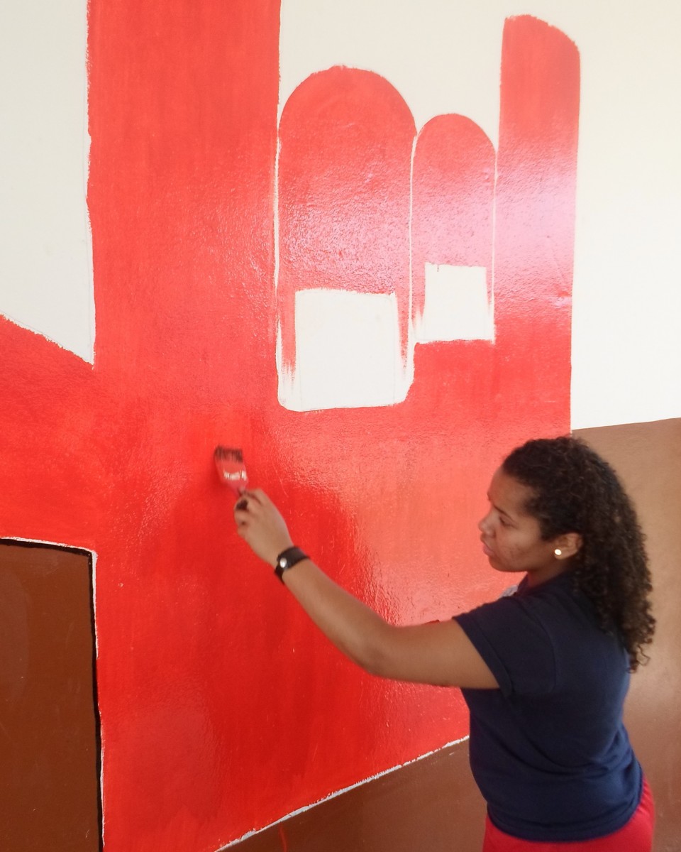 Teresa paints a red hand making the "I love you" hand sign on a wall