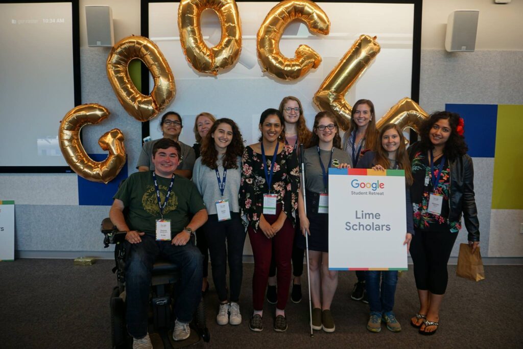 Large group of students, including students with disabilities, pose for camera in front of "Google" balloons and hold a sign that says "Good Student Retreat: Lime Scholars"