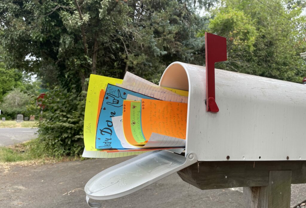 Mailbox with stack of hand-written letters on colorful paper sticking out of the mailbox on a tree-lined street