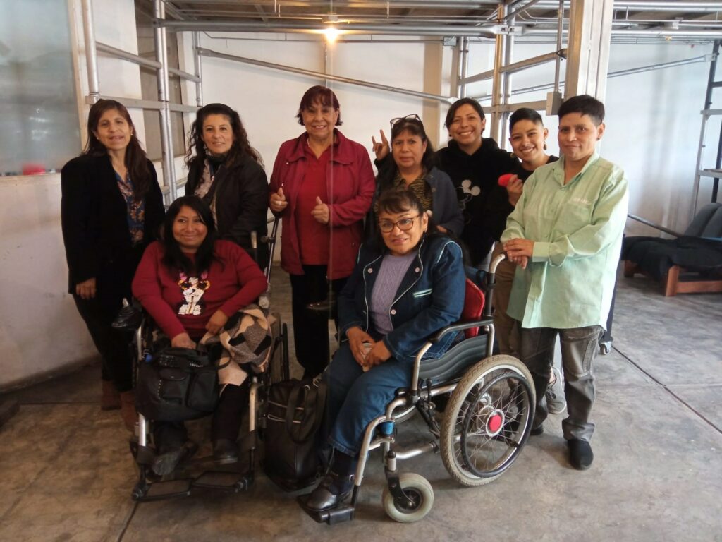 Nine people with various disabilities, some using wheelchairs or crutches, sit and stand together while smiling. 