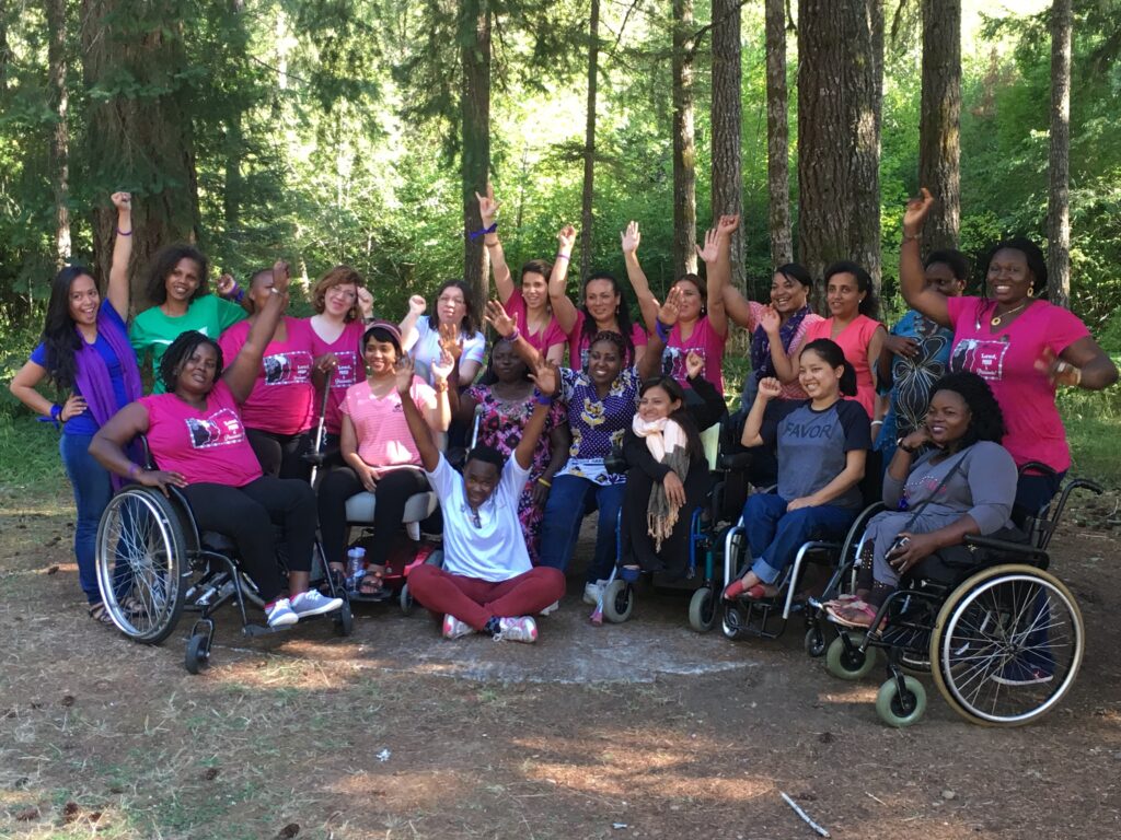 Large group of women of diverse races and disabilities, gathered in a group outdoors. Many wearing hot pink WILD logo t-shirts.